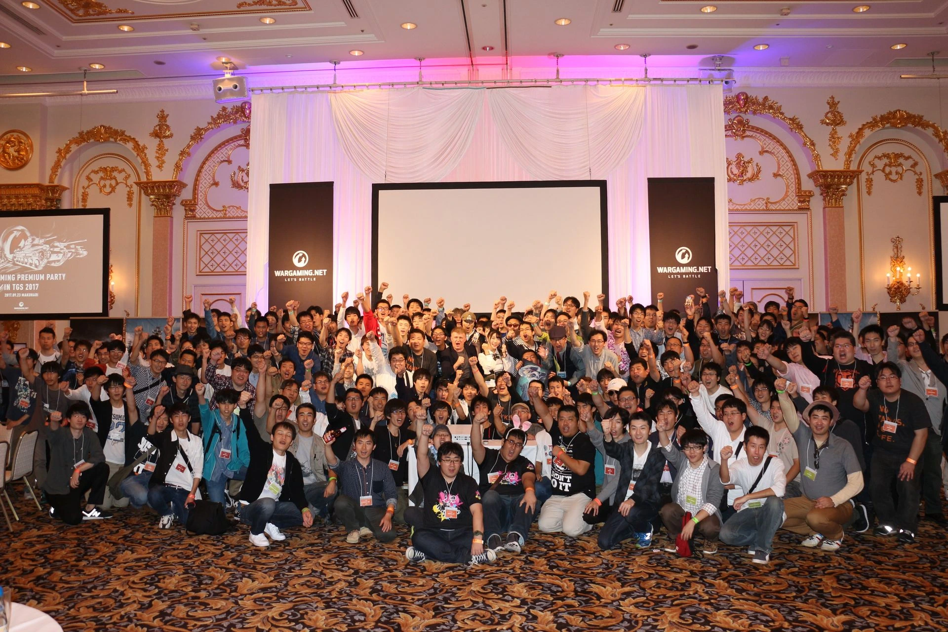 Victor Kislyi speaking at a Wargaming event in a crowded ballroom, with attendees raising their hands behind him